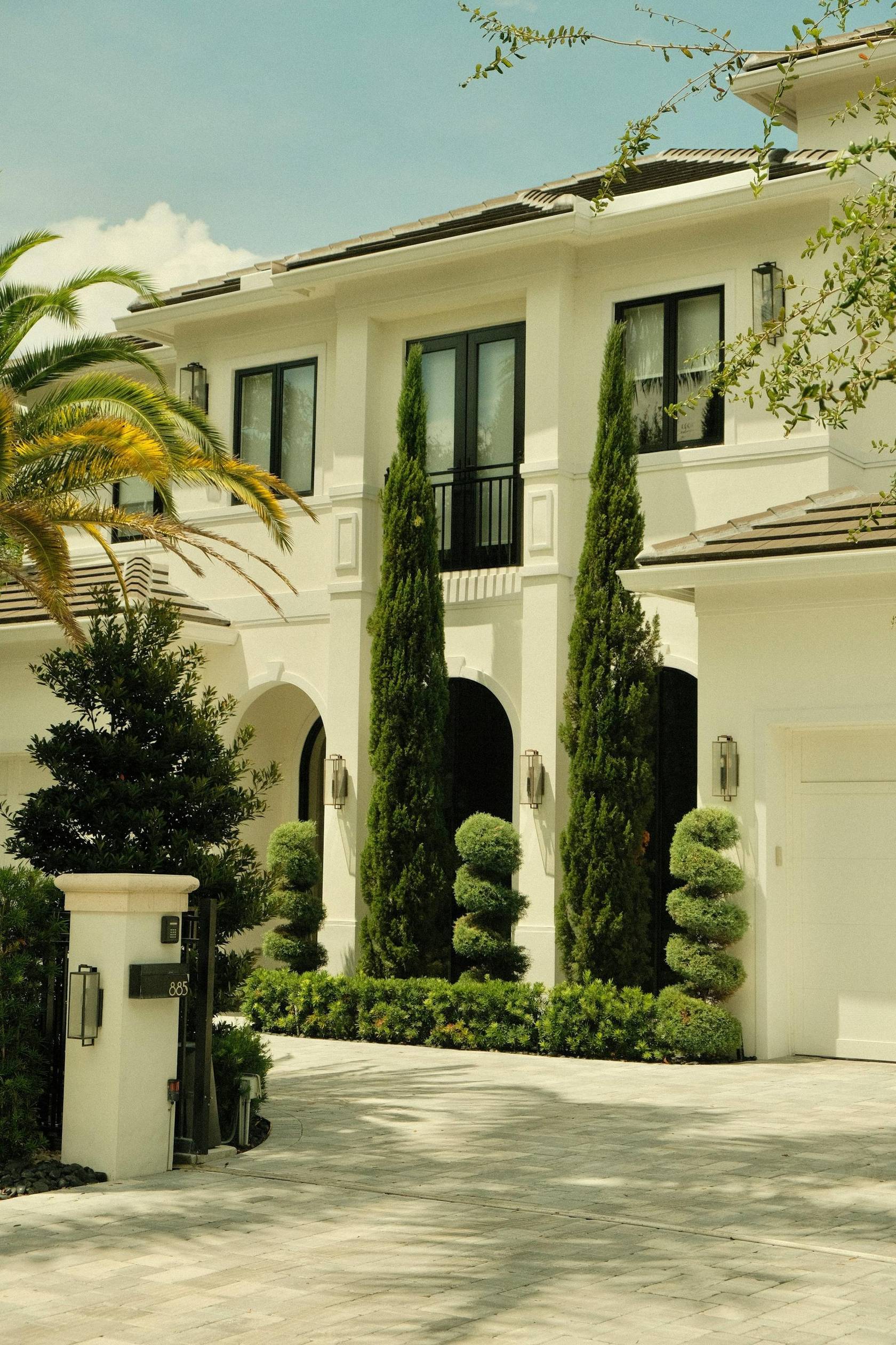 Upscale white South Florida estate home with manicured topiaries and palm trees